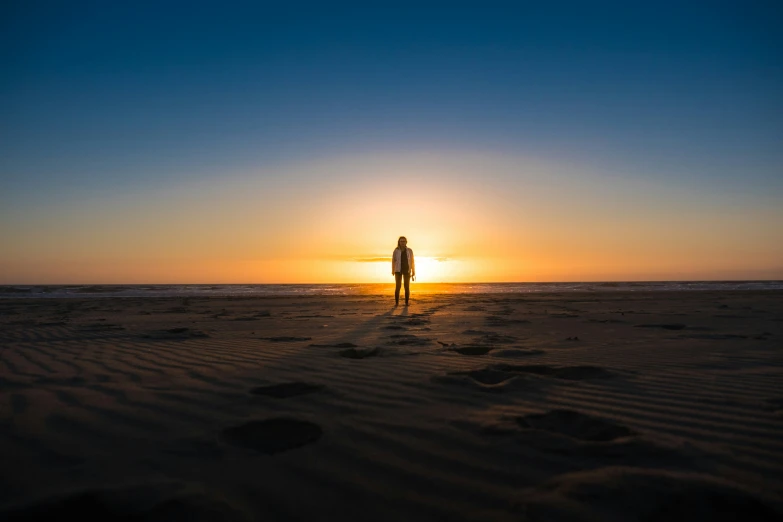 a person standing in the sand with a sun setting behind