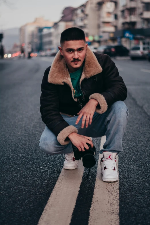 a young man crouches with his shoes on the street