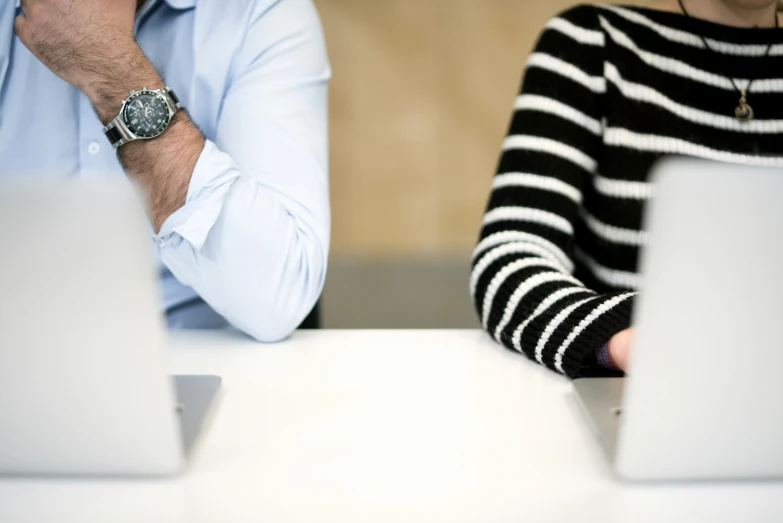 two people sitting at a white table in front of laptops