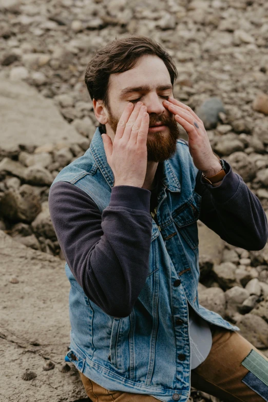 bearded young man with blue denim jacket sitting on the beach