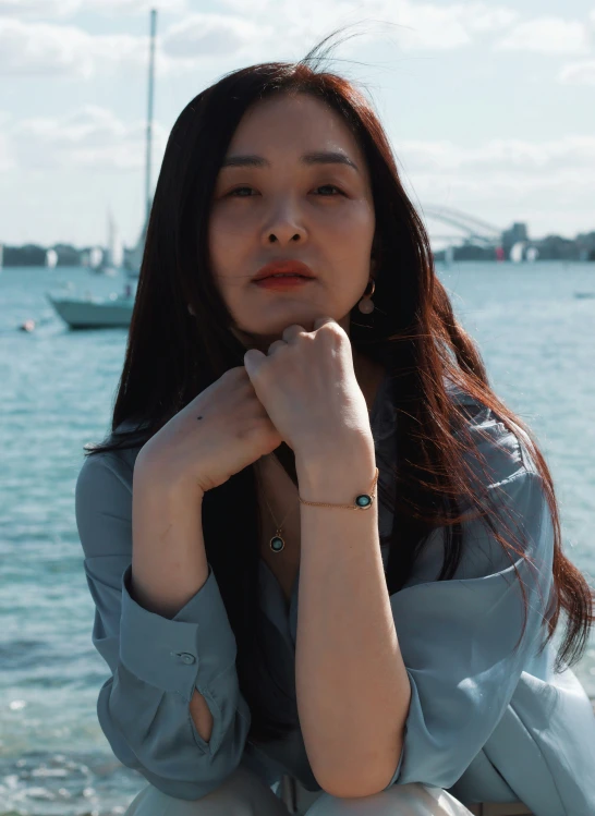 a woman with long hair sitting at the beach looking off into the distance