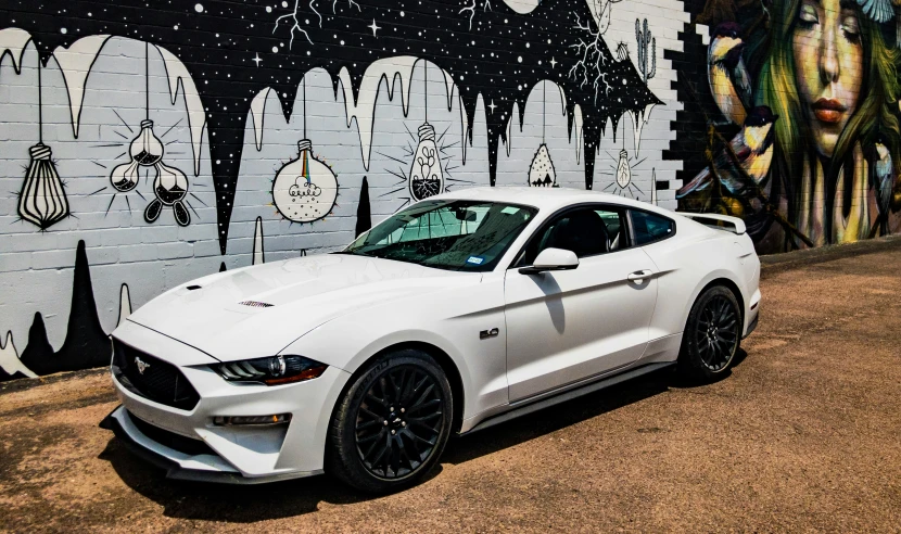 a white mustang parked next to a wall covered in grafitti