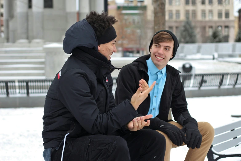 two people in jackets sit on a bench