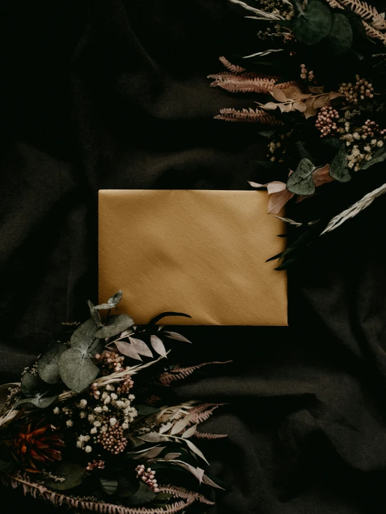 an envelope is laid on a black blanket near flowers
