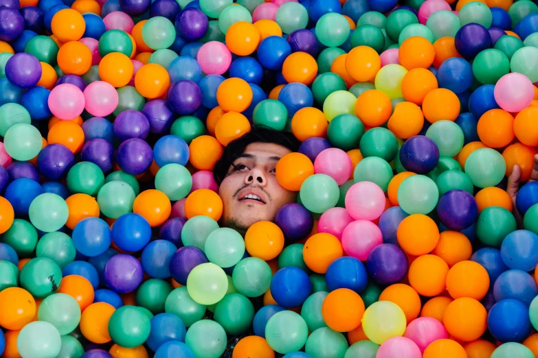 a boy laying in ball pit with his head out