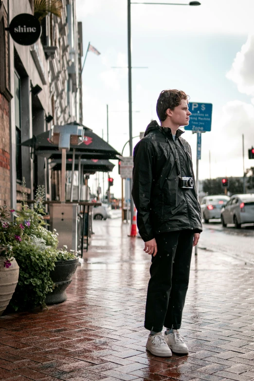 a boy stands in the rain wearing black jacket and sneakers