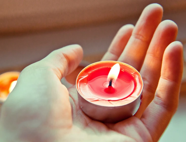 a small red candle is glowing next to a person's hand