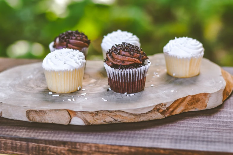 three chocolate and white frosted cupcakes on a wooden serving tray