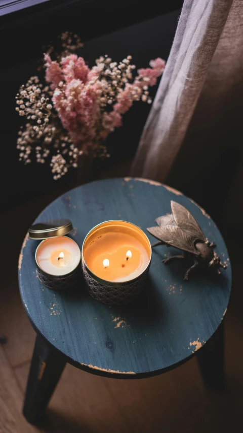 two candles sit on a table with a flower arrangement behind them
