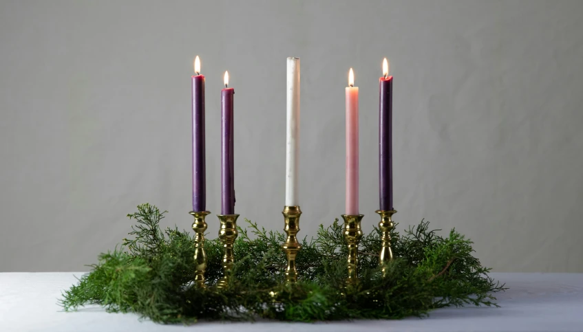 three candles in a candle holder with some greens on it