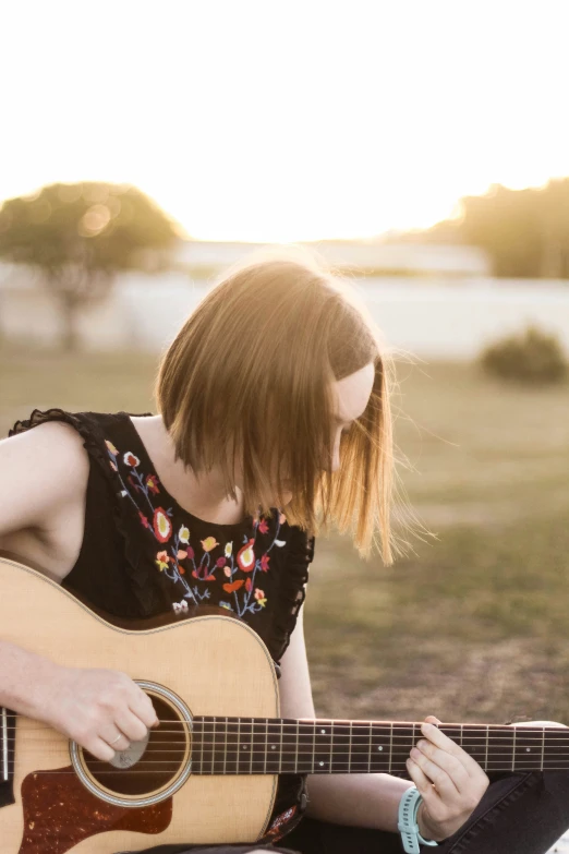 a girl sitting in the sun with an acoustic guitar