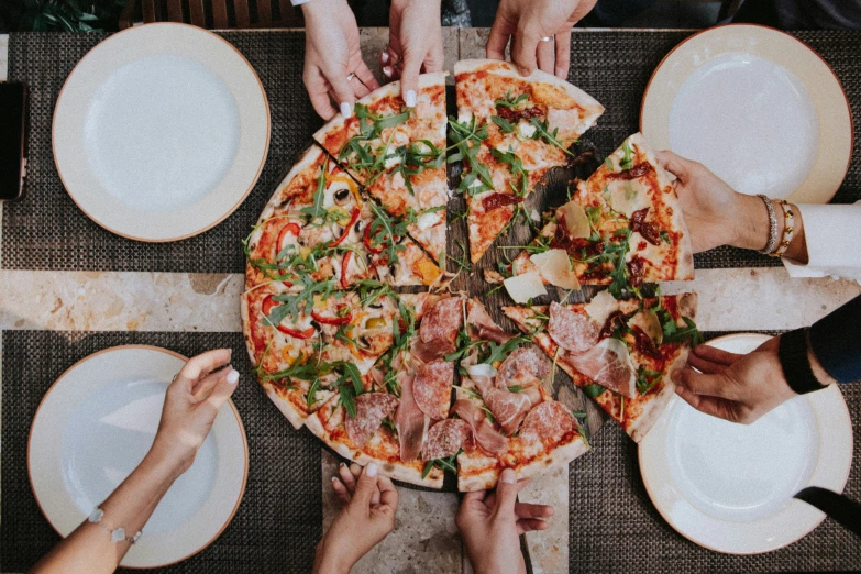 the people are eating pizza together and grabbing their hands