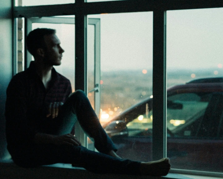 a man sitting in a window sill looking out the window