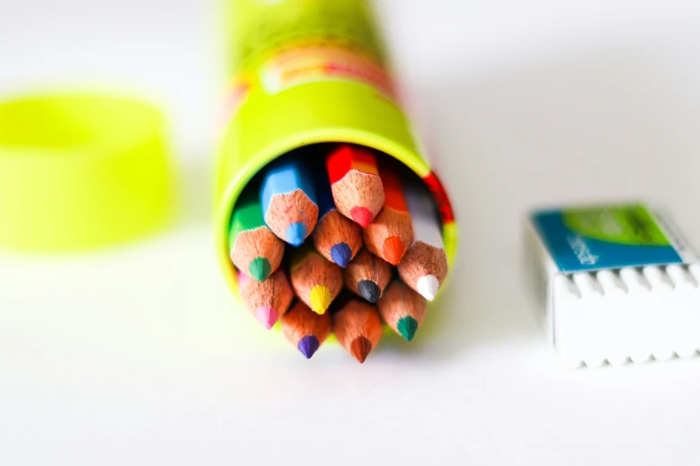 a stack of brightly colored crayons sit together next to a white and green cup