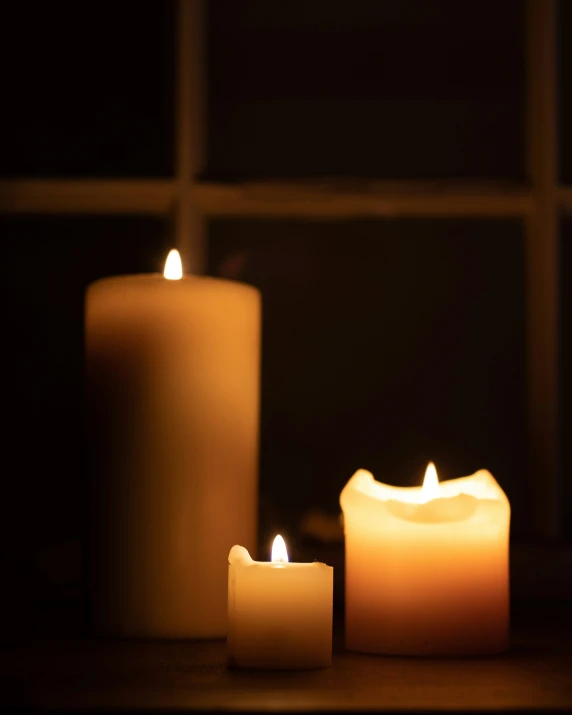 three candles glowing in front of a window with a lit curtain