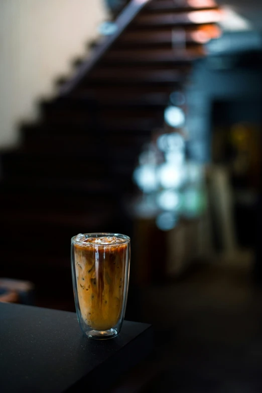 a close up of a glass of drink with a staircase behind it