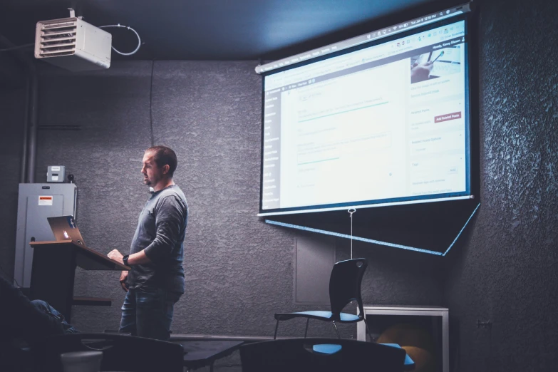 a man standing in front of a large screen giving a presentation