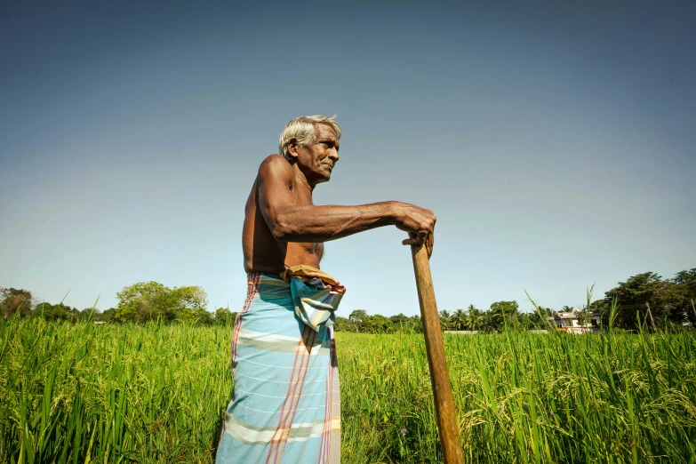 an old man is standing in a field with a stick