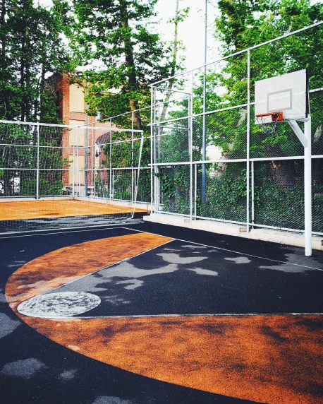 an outdoor basketball court surrounded by fence and green trees