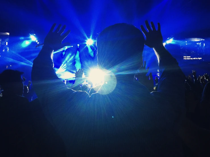 person in dark stage lighting raising hands with bright beams