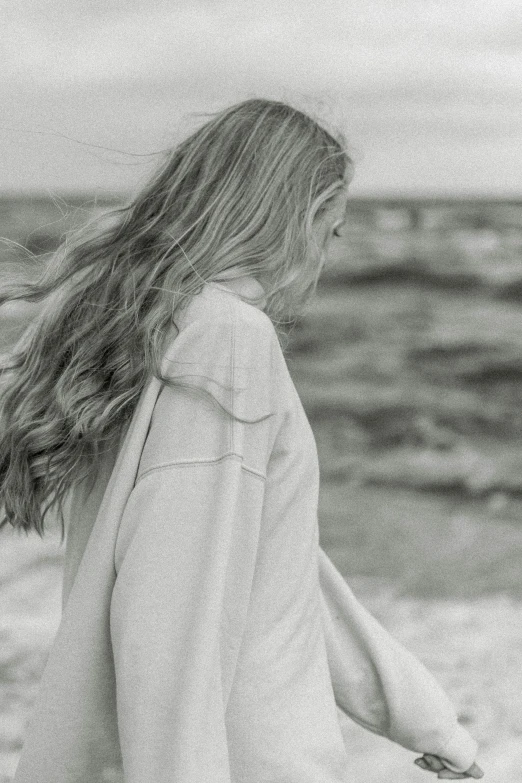 woman in jacket and jeans walking on beach next to ocean