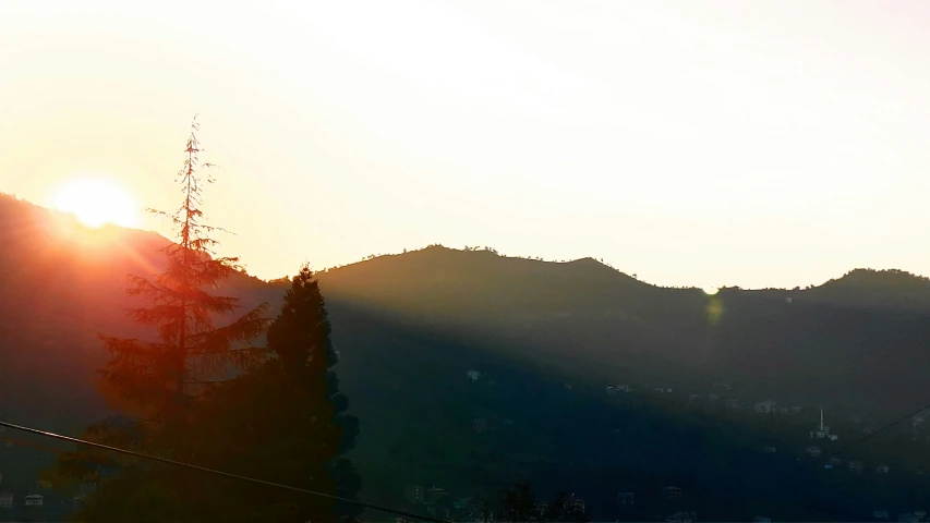 the silhouette of the mountains and trees with sun in background