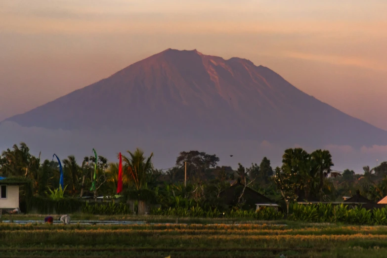 a large volcano looms over the city at sunset