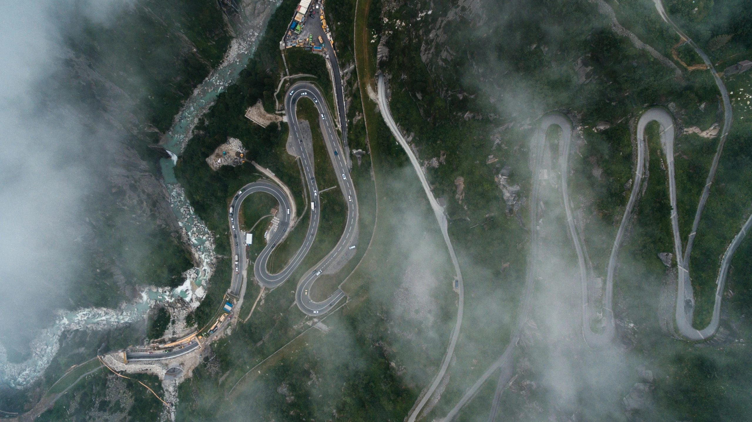 aerial view of road curves and trees near a cloudy sky