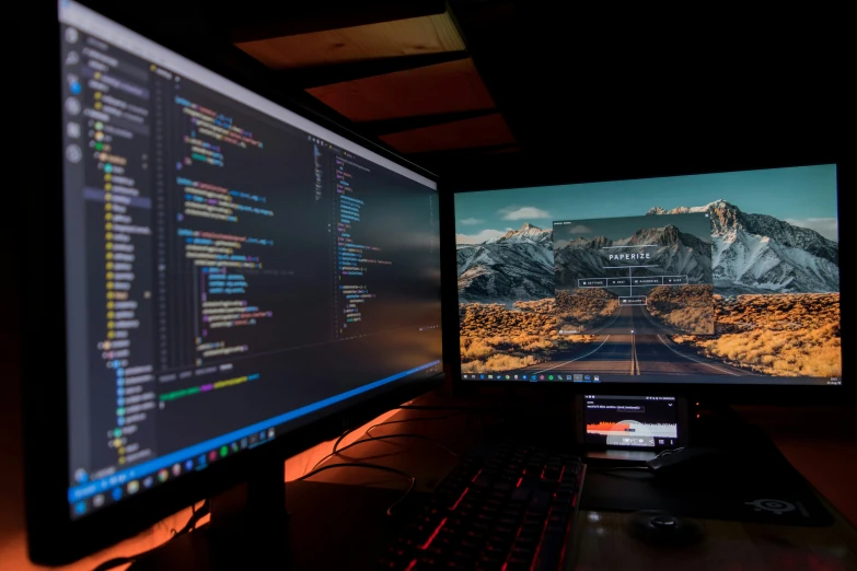 two computer monitors are seen together on a desk