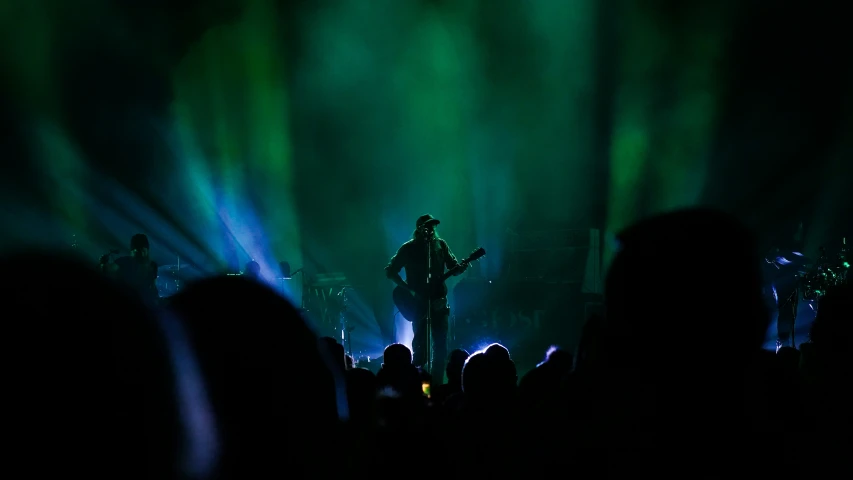 a musician playing guitar in front of the light of the stage