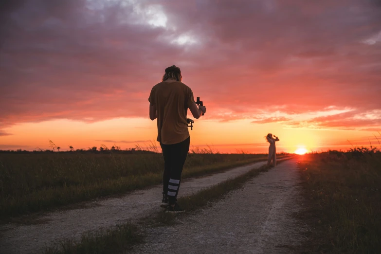 a couple of people walking down a dirt road next to grass