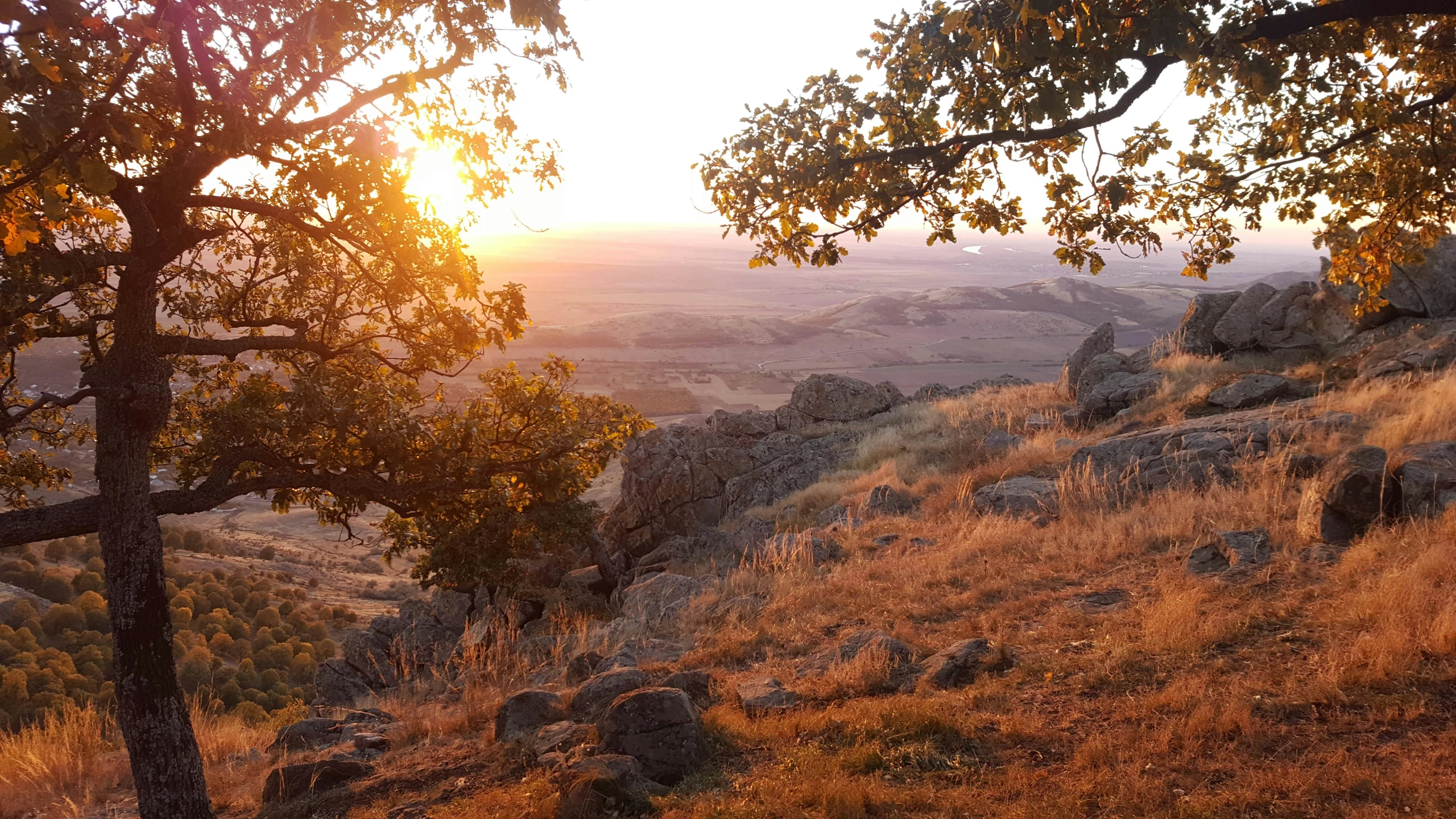 a sun set on the mountain with a grass slope