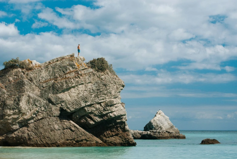 person on rock formation overlooking crystal clear water