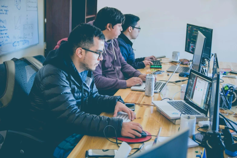 people sitting at a desk with many computers on them