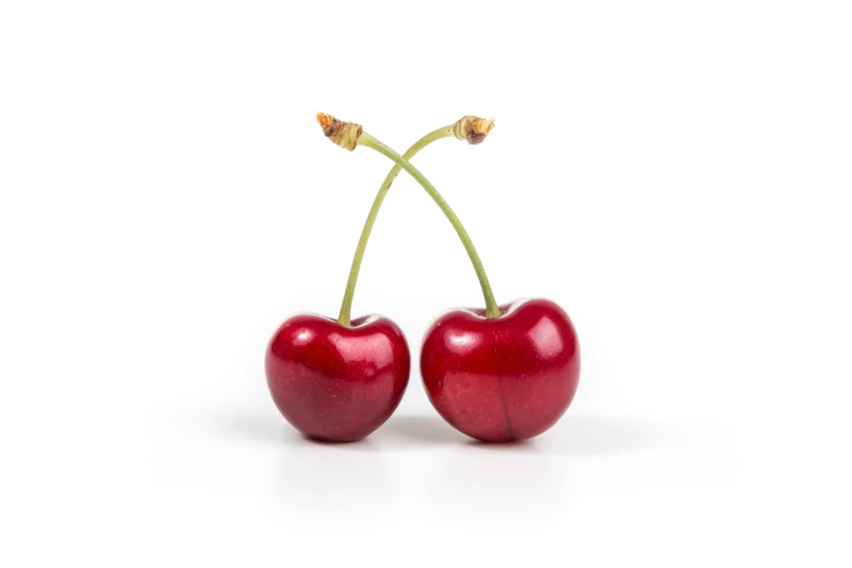 two cherries sitting on top of each other on a white surface