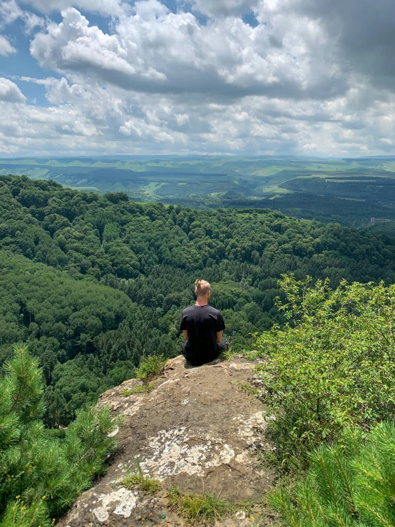 a man sitting on top of a mountain looking out at a valley