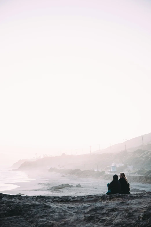 two people sitting on a bench by the beach