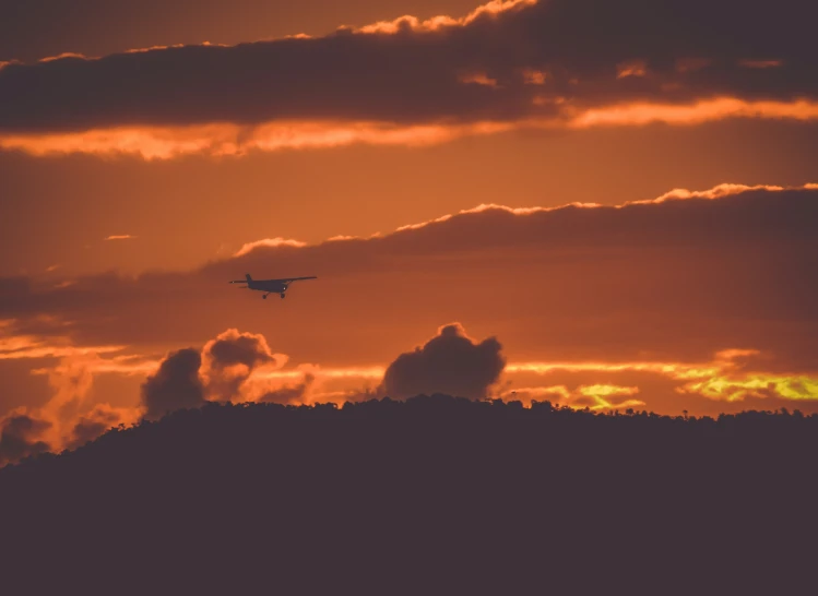 a plane flying over the top of a mountain at sunset