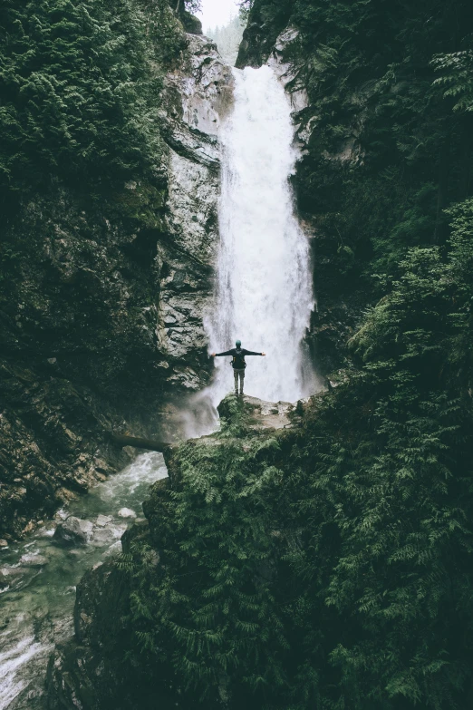 man standing in front of water fall, with hands raised, and looking down