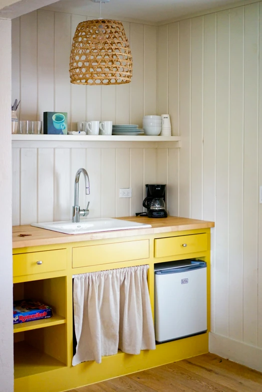 a small yellow kitchen has a white sink and yellow cabinetry