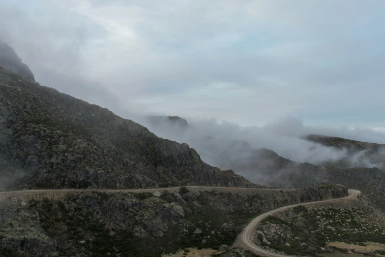 a mountain road on the side of the road with clouds moving overhead