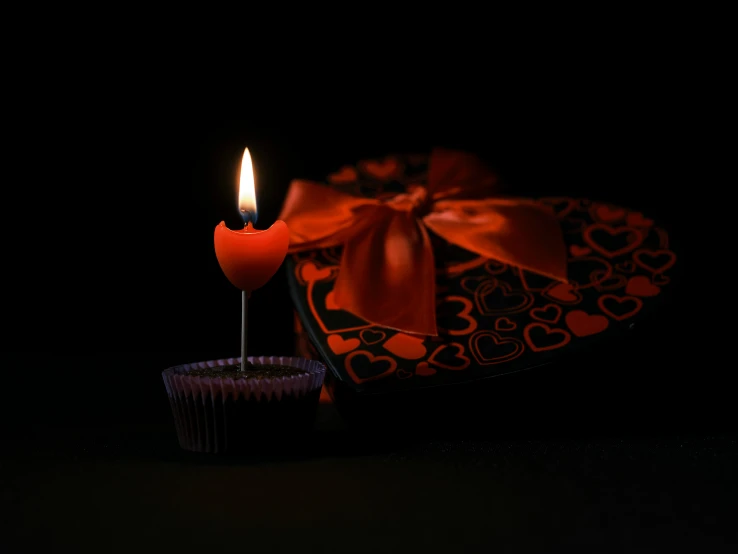 a single burning candle next to a chocolate cupcake