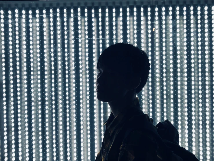 a silhouette of a man with his back turned to the camera in front of a background of glowing, cylindrical lights