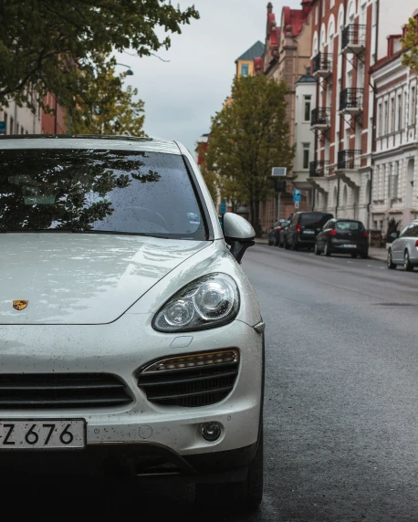 the front end of a silver porsche cayen parked on the side of a street