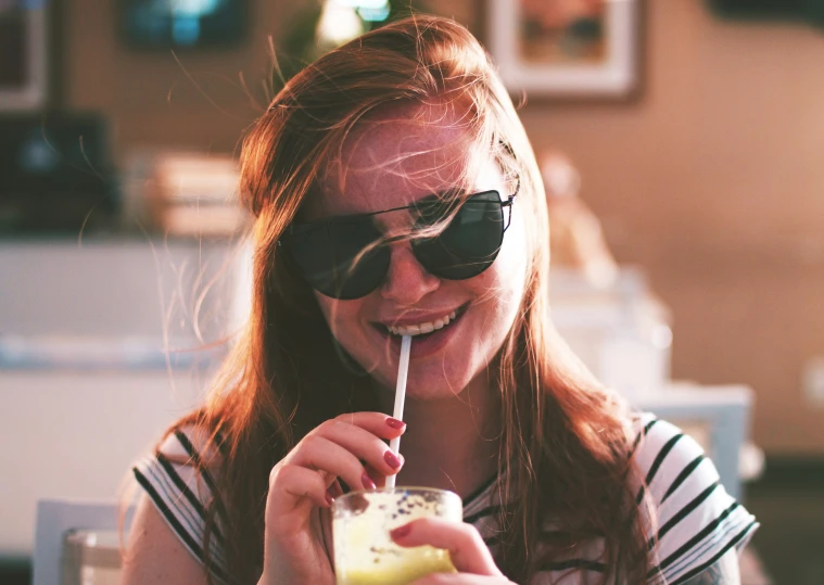 a woman in glasses holding a drink up to her face