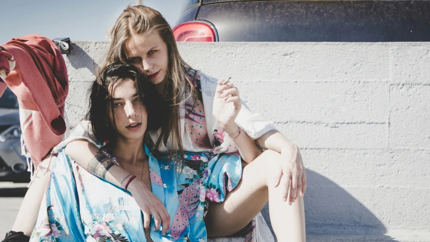 two girls in a parking lot next to a car