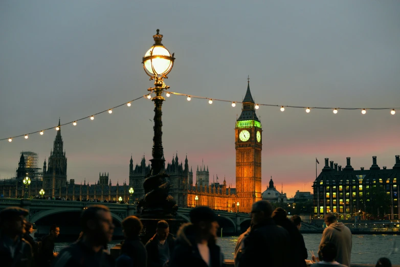 people standing on a pier at night, with a clock tower in the background