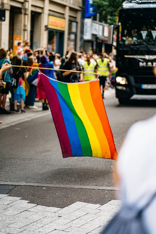 a large rainbow flag that is attached to a line of people on the side walk