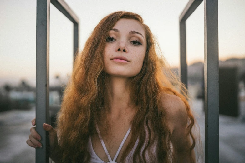 a young woman stands behind bars with her red hair flowing over her head