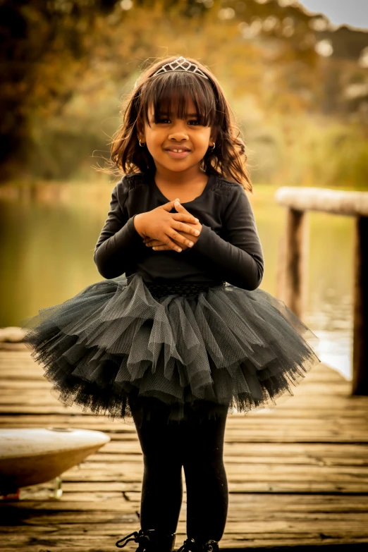 a little girl in a black dress is standing on a wooden bridge